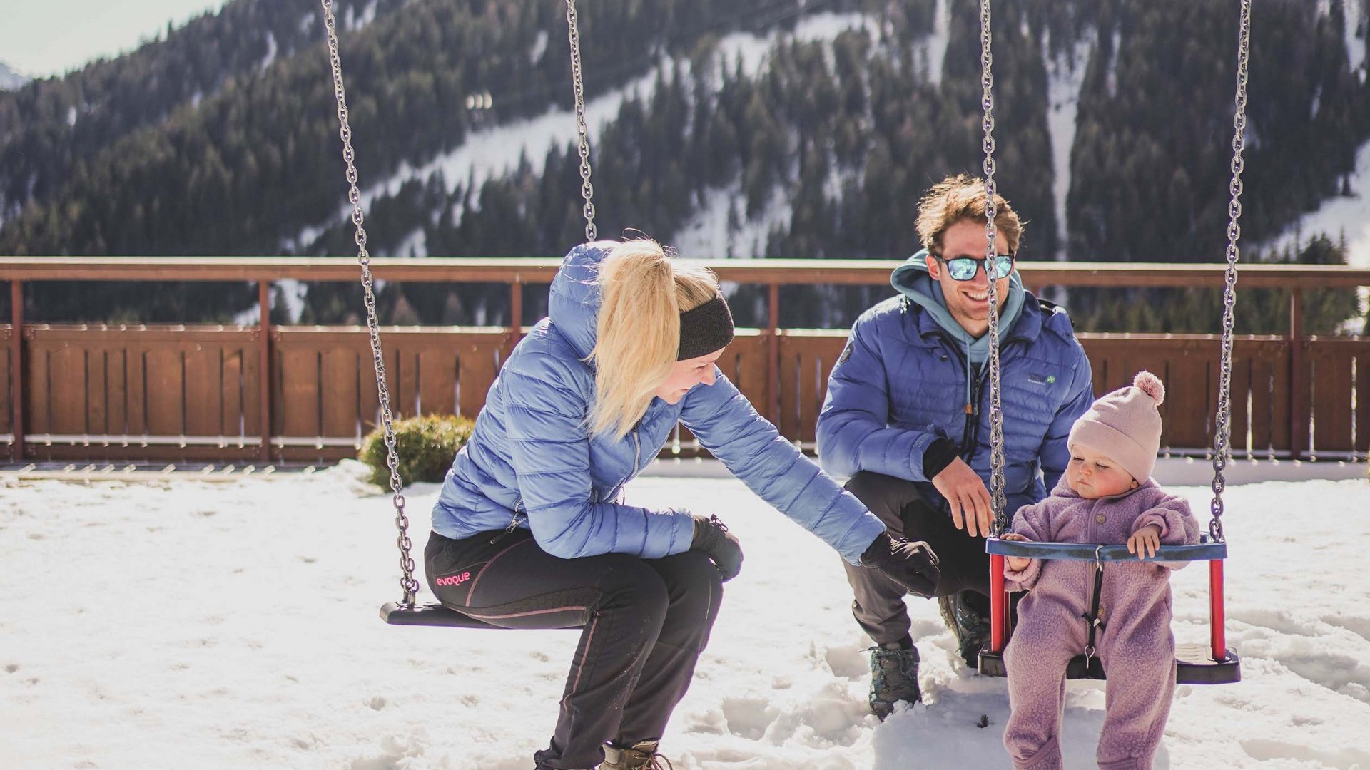Familie spielt auf Schaukel im Schnee mit Bergkulisse