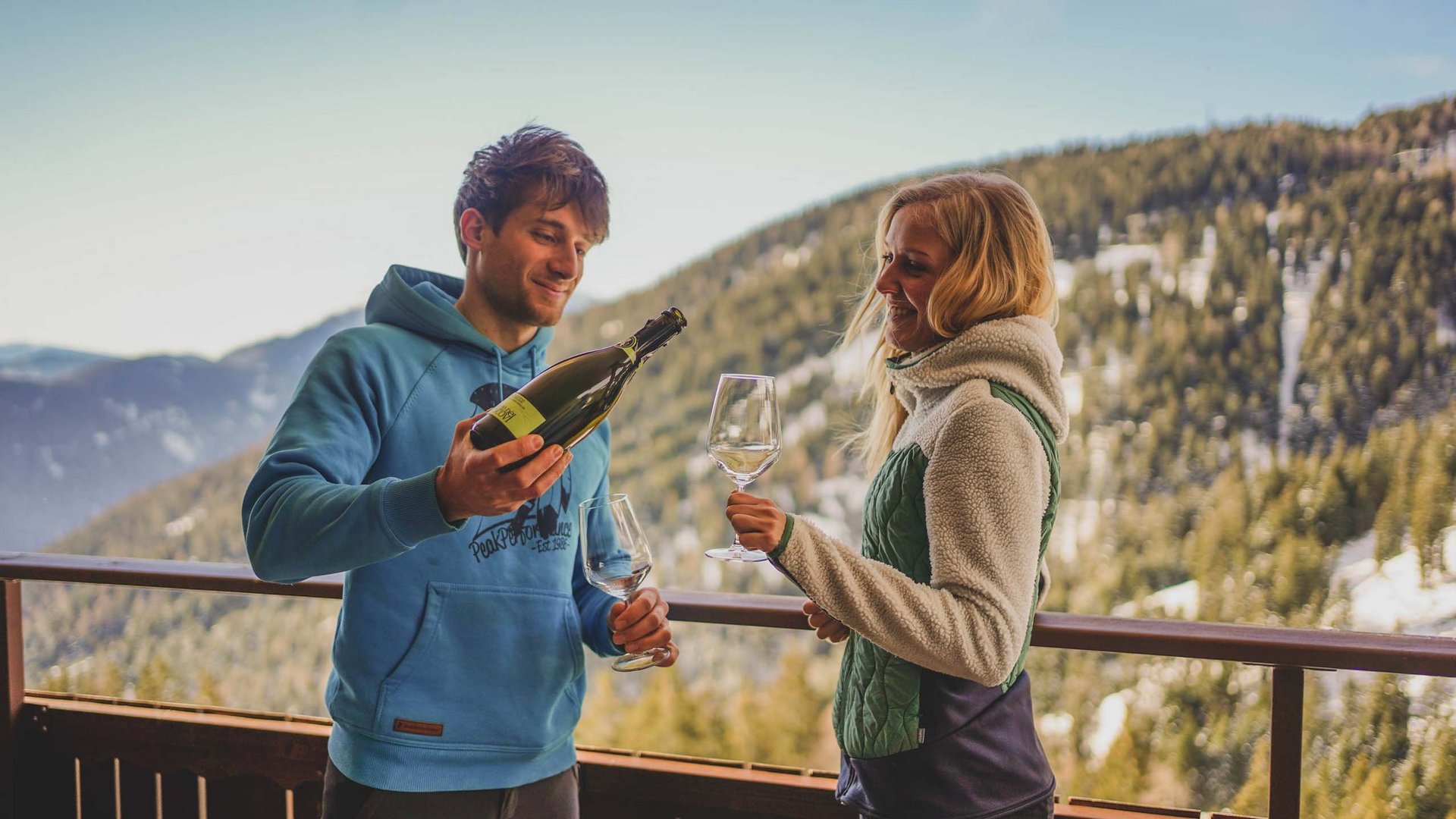 Coppia su balcone in montagna con vino e bicchiere in mano